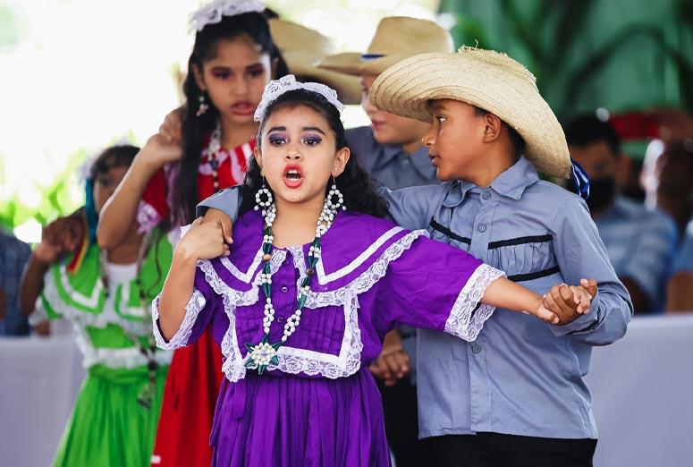 Young children dancing in festive cultural clothing at outdoor festival event.